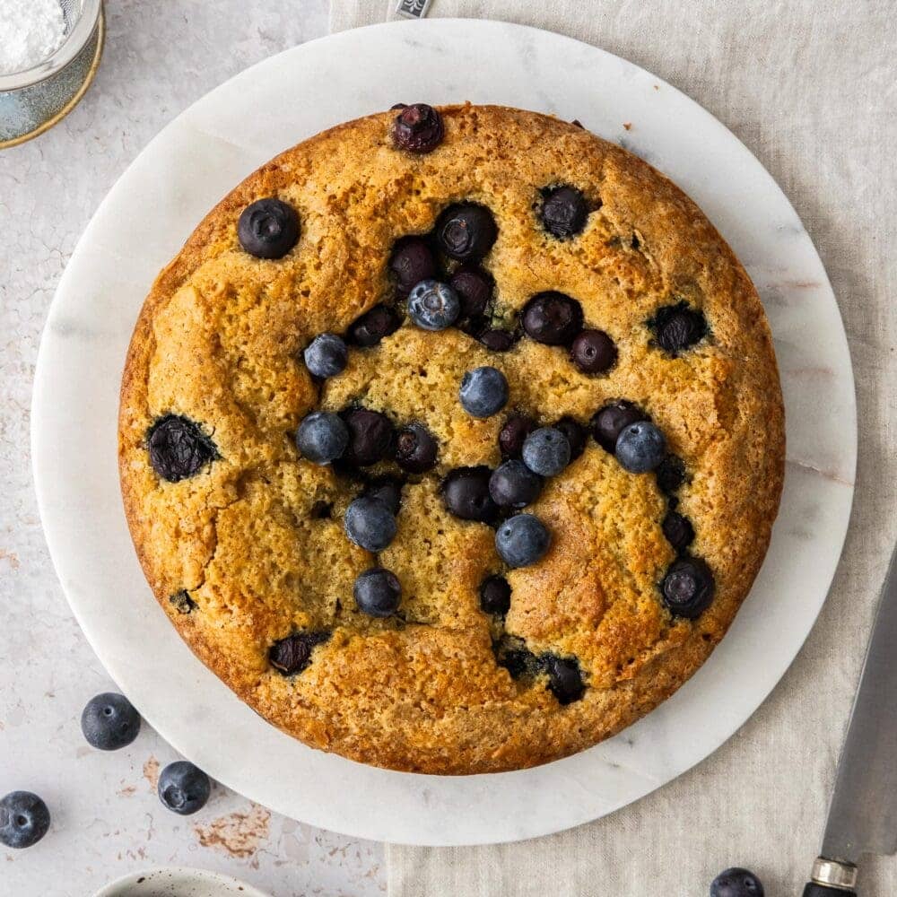 Top down view of a round cake studded with blueberries.