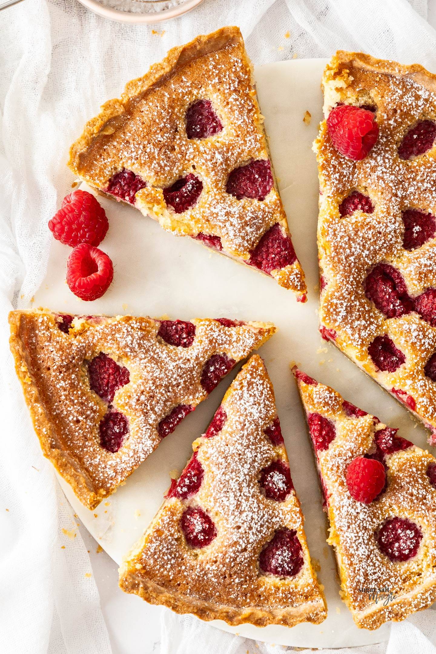 Top down view of a raspberry frangipane tart cut into slices.