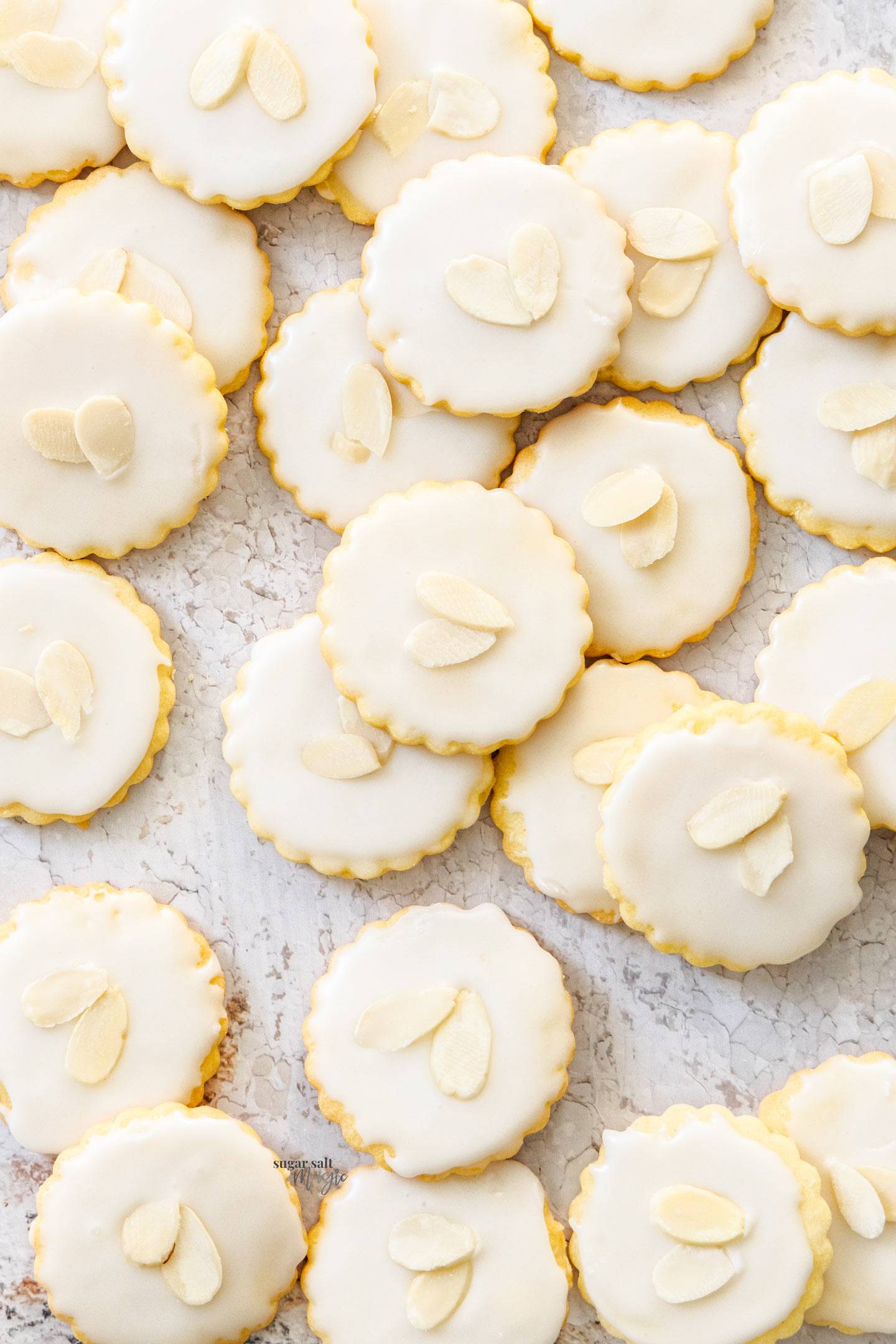 Top down view of a batch of almond cookies topped with icing and almonds.