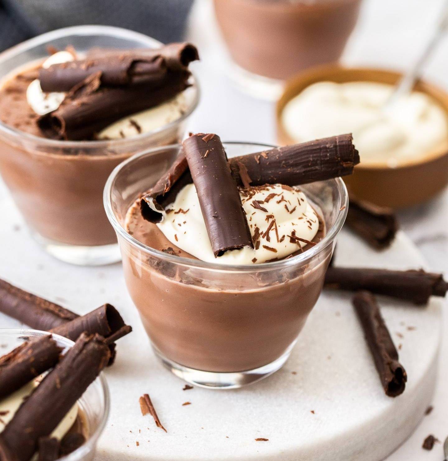 Two small glasses filled with chocolate pudding, topped with cream and chocolate curls.