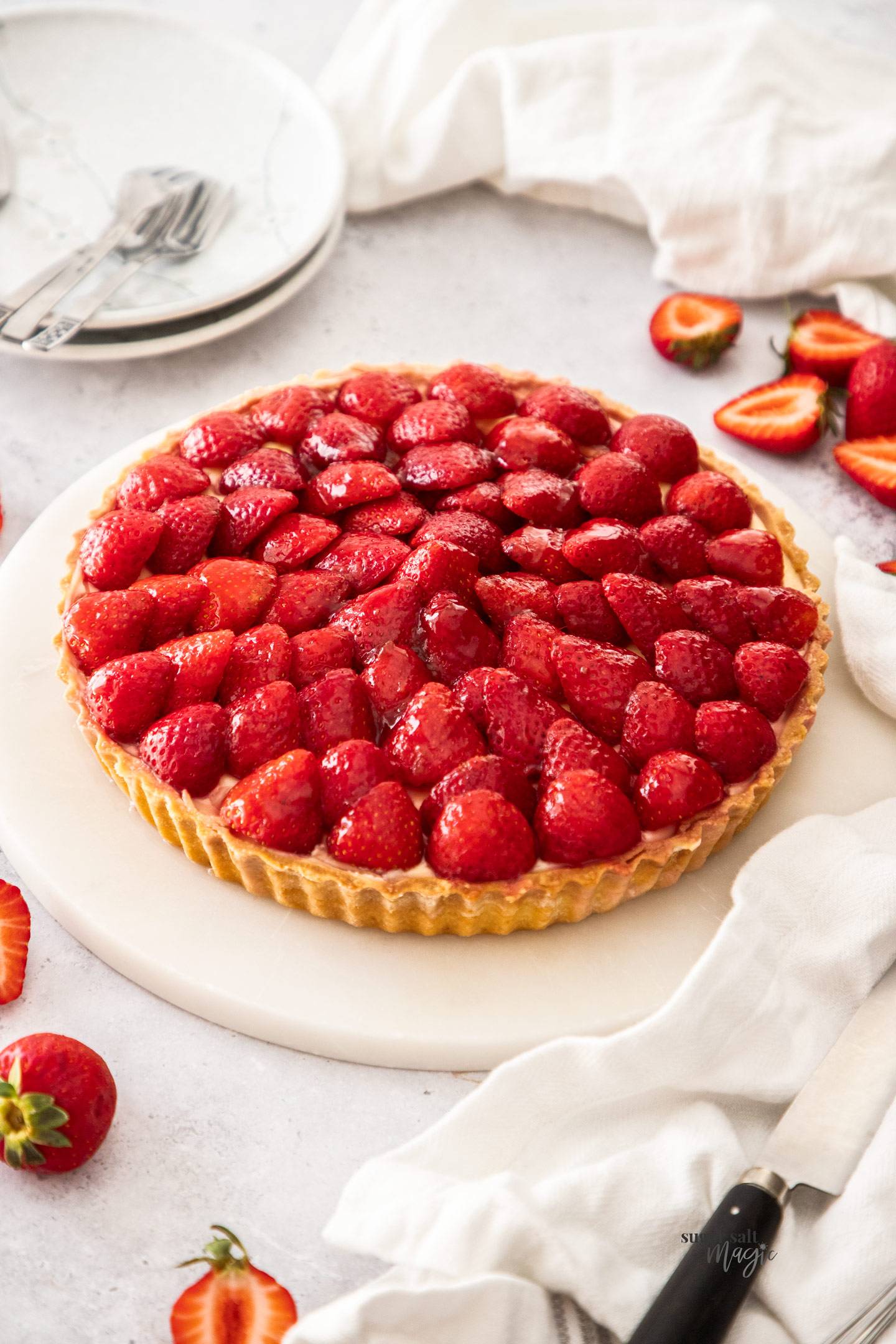 A whole strawberry custard tart on a marble platter.