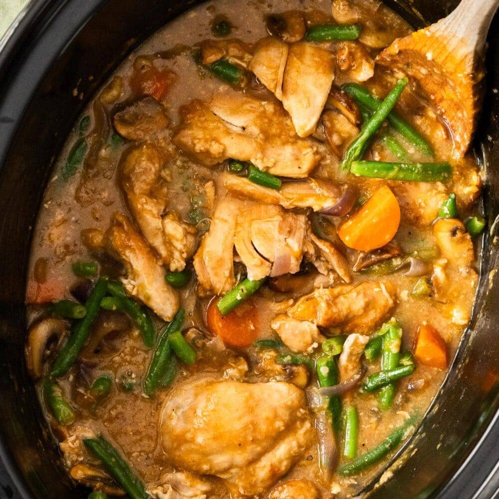 Top down view of a slow cooker filled with chicken and vegetables in an apricot sauce.