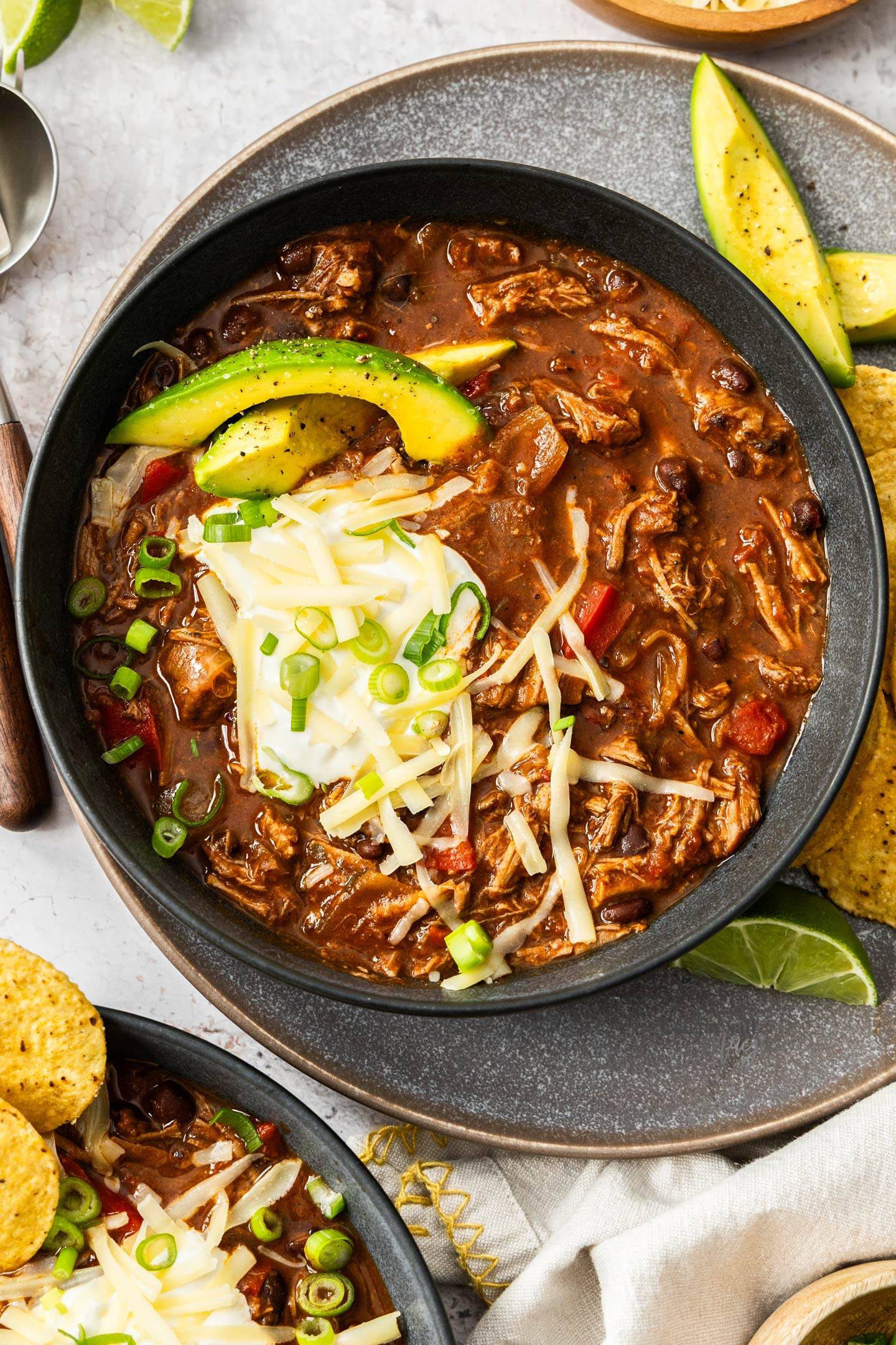Top down view of a bowl of chili con carne topped with sour cream and avocado.