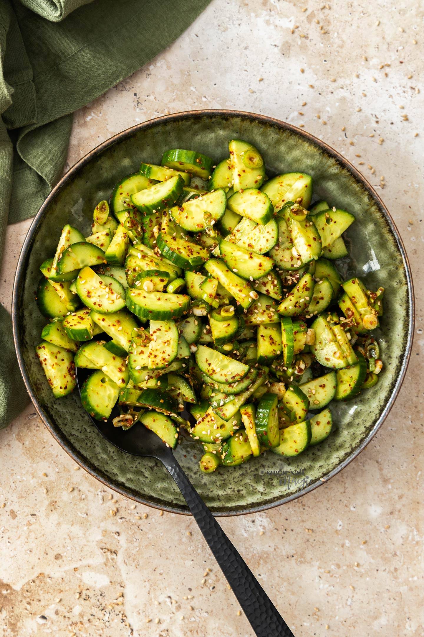 Top down view of a cucumber salad in a bowl on a stone surface.