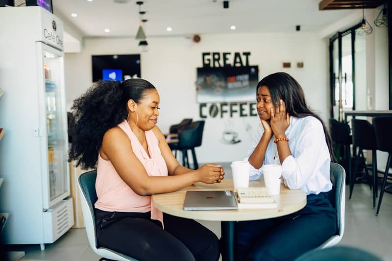 A couple of women sitting at a table with a laptop