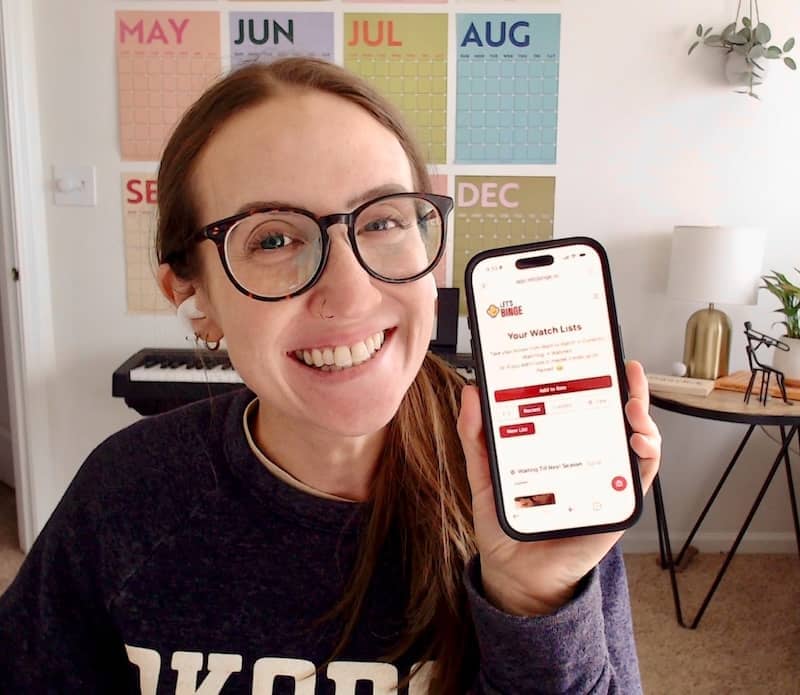 Hayley holding a phone with the Let's Binge app on it