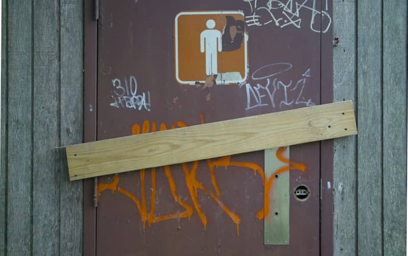 A brown door with a restroom sign and orange graffiti boarded shut