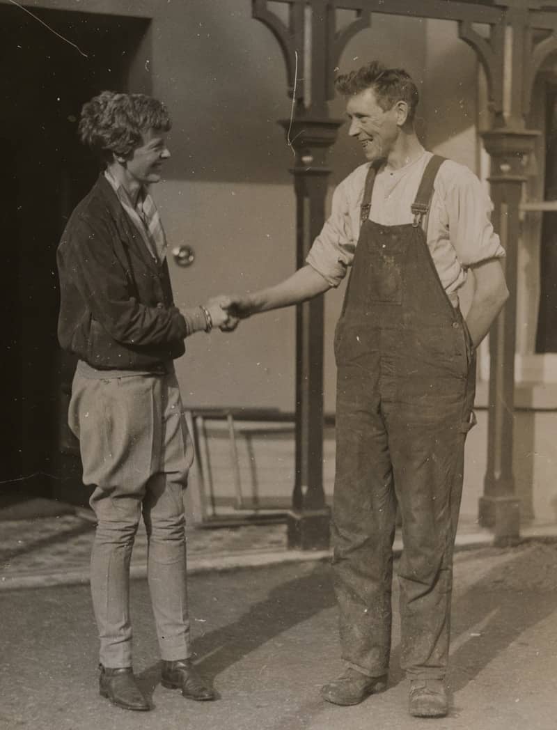 Man in overalls shakes hands with woman in riding attire.