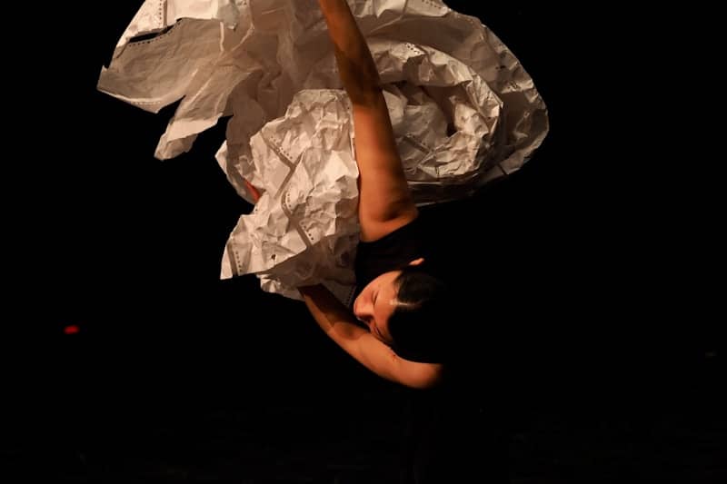 A dancer in a white costume hangs upside down.