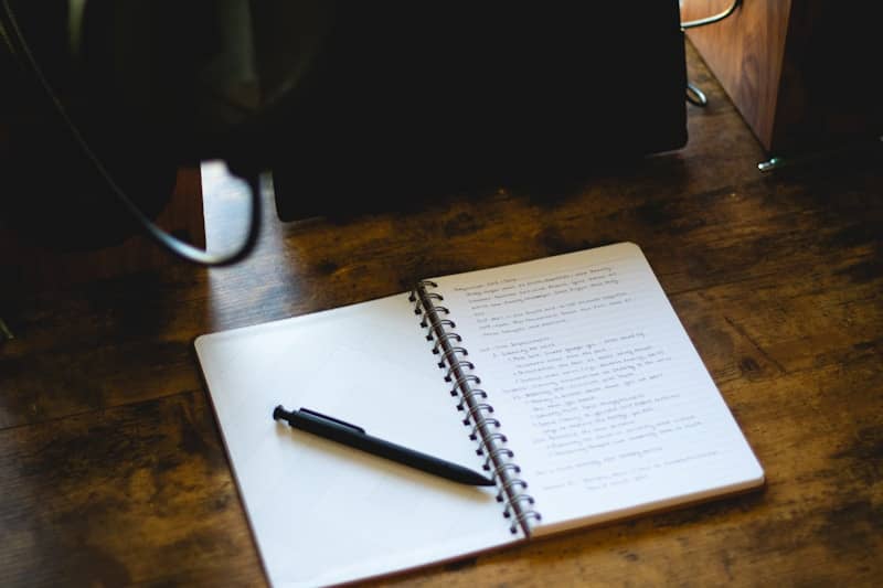 An open notebook with a pen on a wooden desk.