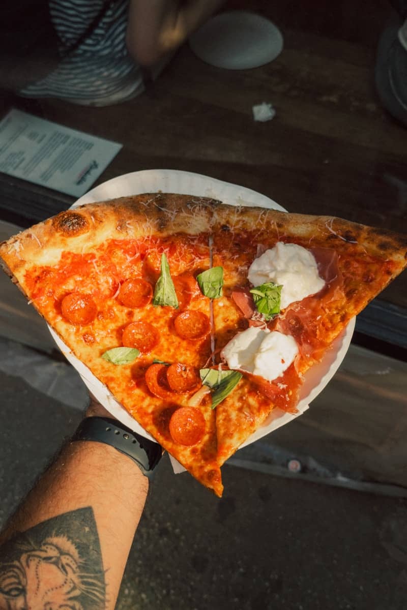 Hand holding a delicious pepperoni and fresh mozzarella pizza slice.