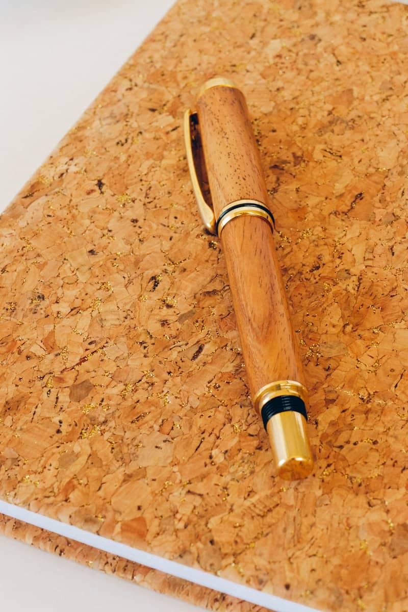 Wooden pen rests atop a cork notebook.