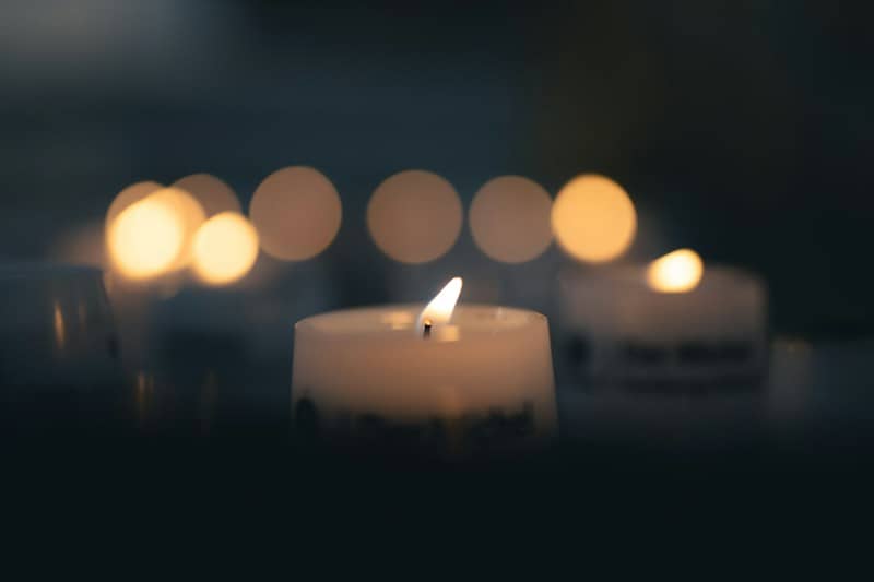 A single lit white candle with a soft bokeh of golden lights in the background