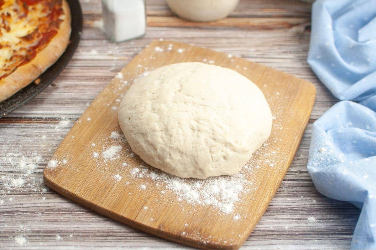 Sourdough pizza dough on wooden cutting board.