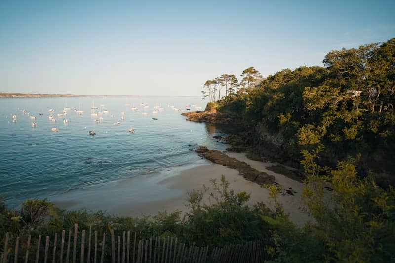 Scenic bay with boats, sandy beach, and green cliffside.