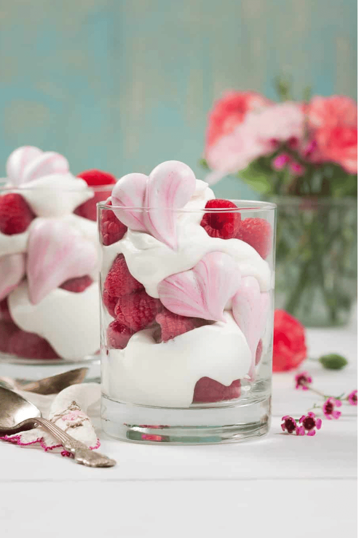 A glass filled with meringue hearts, cream, and raspberries. 
