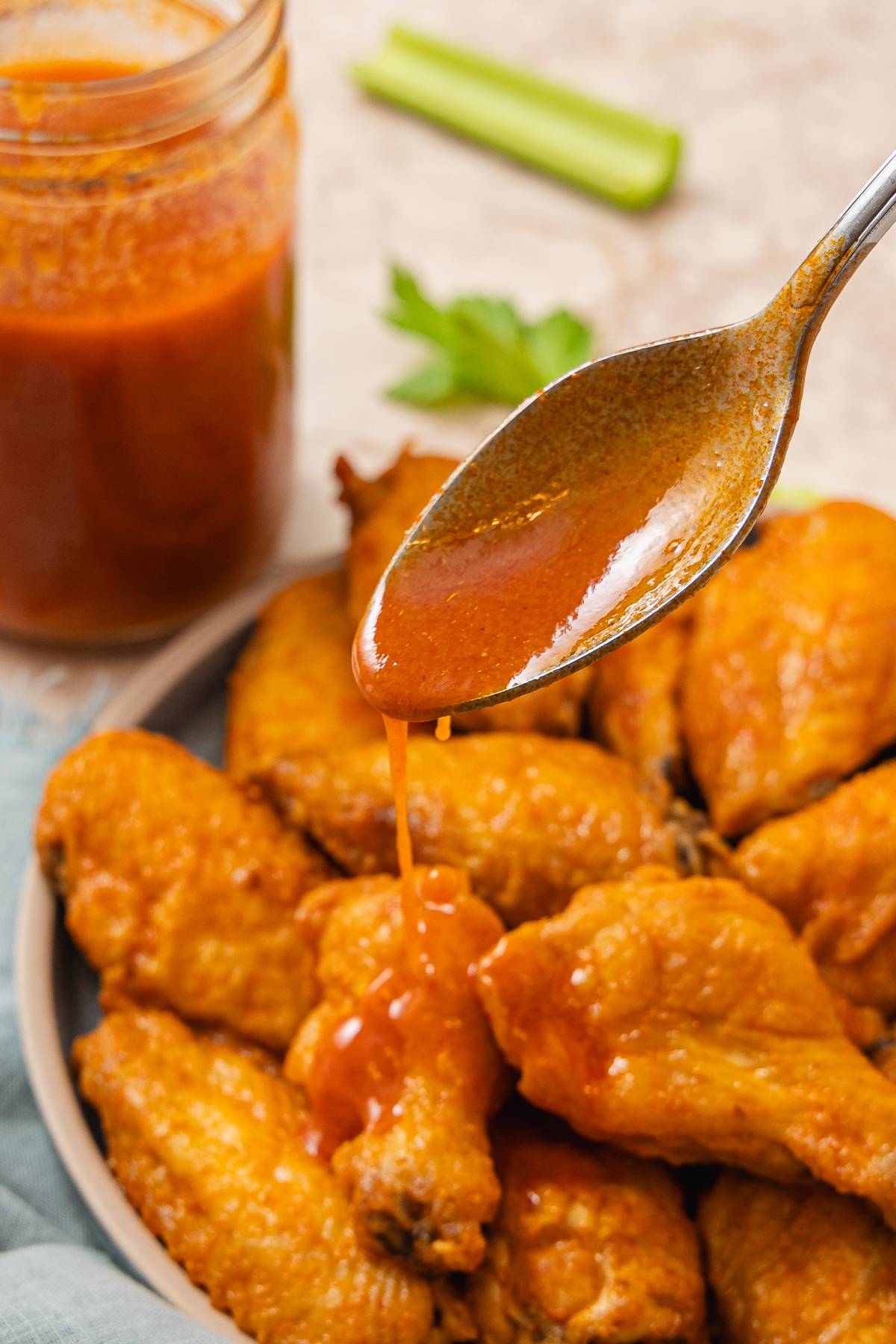 A spoon slowly drizzling a red sauce on top of chicken wings. 