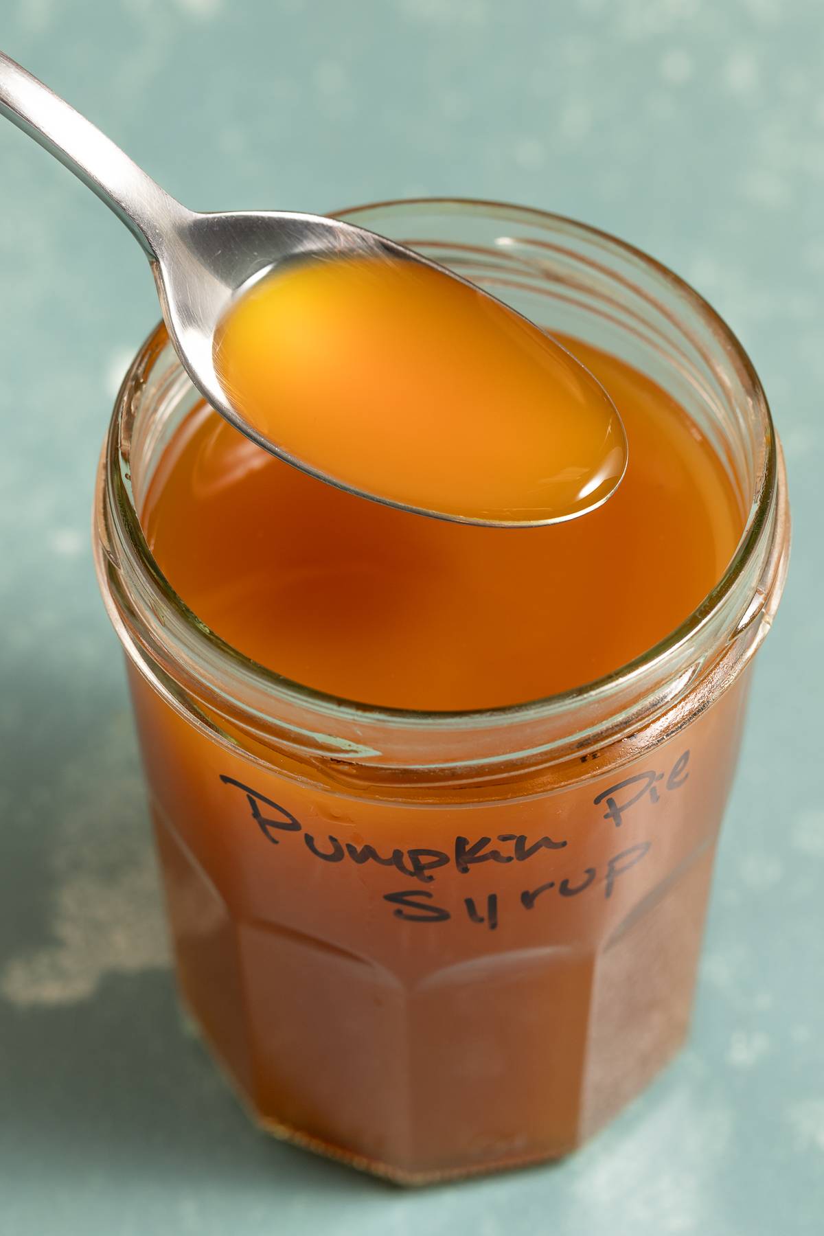 a spoon of orange syrup held above a jar with the same colored liquid. 