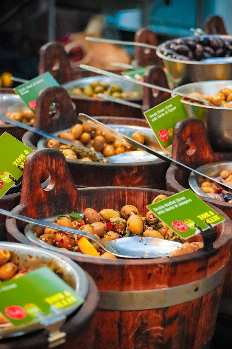 Variety of marinated olives in wooden barrels at market.