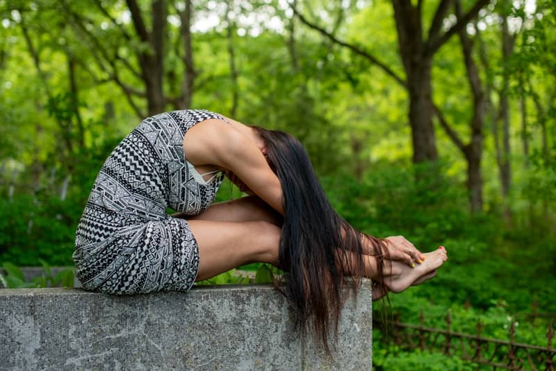Woman in dress stretching on concrete ledge outdoors.