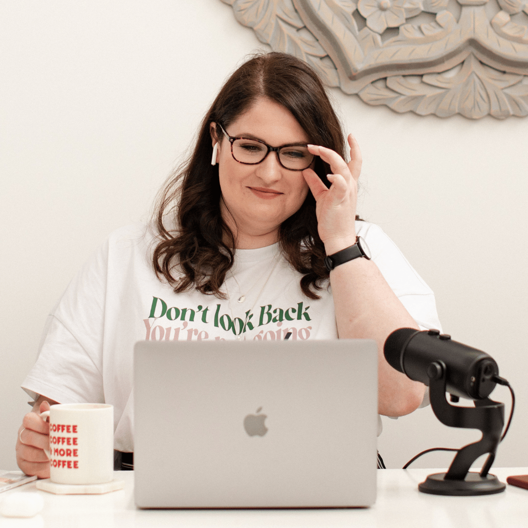 Photo of Emma looking at computer and holding a coffee mug. A microphone is on the table