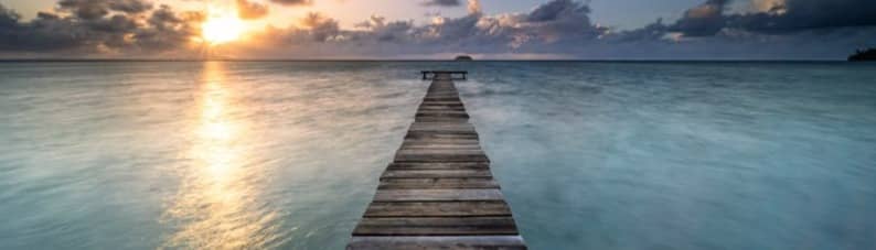 a wooden pier extending into the ocean at sunset