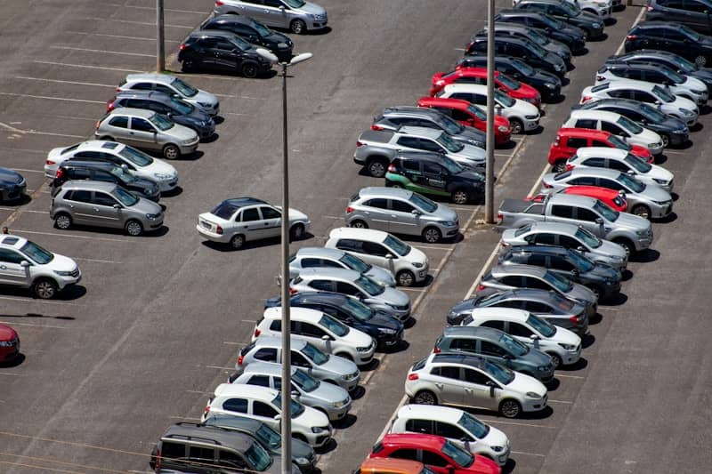 cars parked on parking lot during daytime, with one car out of a space in the lane of travel